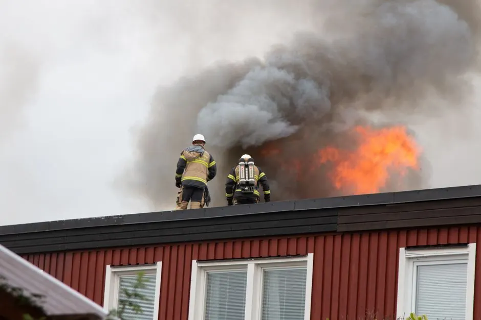 Firefighters tackling a rooftop blaze with smoke and flames in Stockholm. Emergency response scene.
